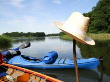 Symbolfoto Freizeit - Kanus auf dem Wasser und Strohhut auf einem Stock