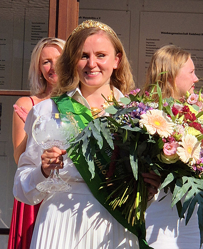 Weinkönigin in weißem Kleid mit Blumenstrauß und Weinkelch