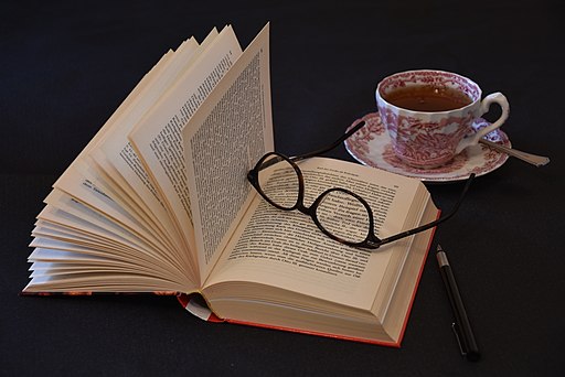 Aufgeschlagenes Buch mit Brille, Stift und Teetasse